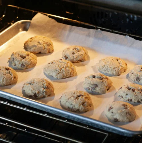 Chocolate chip cookies baking on parchment paper-lined tray inside an oven
