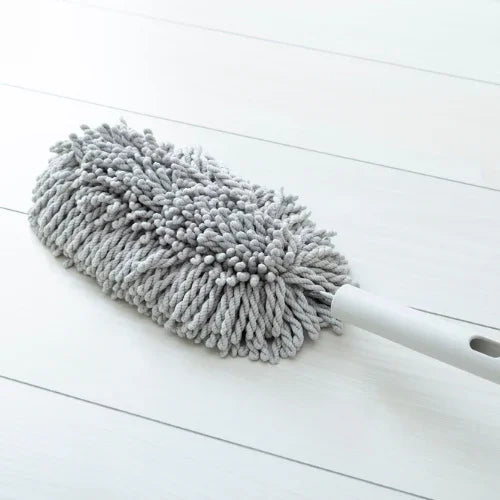 Gray microfiber chenille duster with white handle on white wooden floor